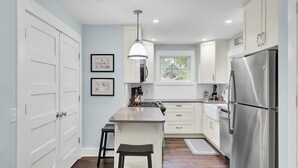 Una cocina moderna con armarios blancos, un refrigerador de acero inoxidable y una isla central con taburetes.