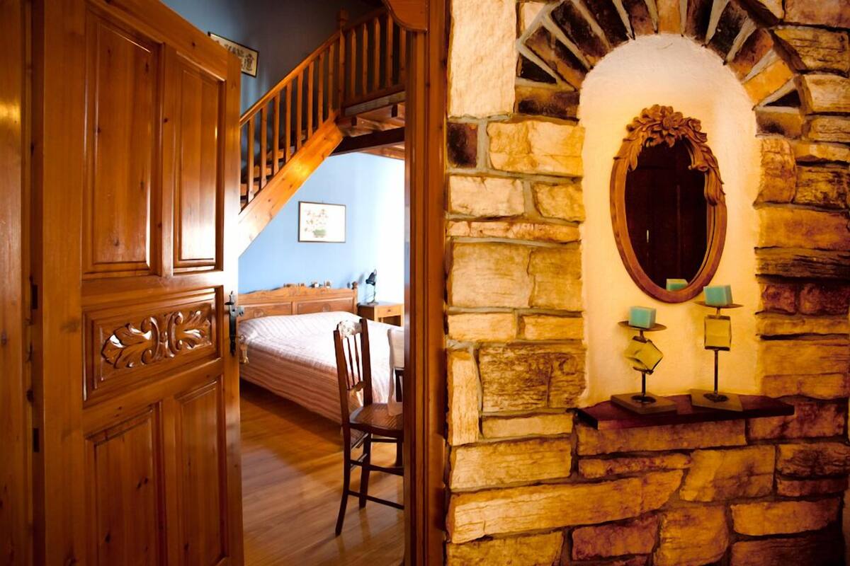 A wooden door leading to a bedroom with a bed, a chair, and a staircase.