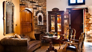 A cozy living room with a stone wall, a wooden sofa, a round table with a bowl, and a wooden chair. - Archontiko Panagoula (Volos)