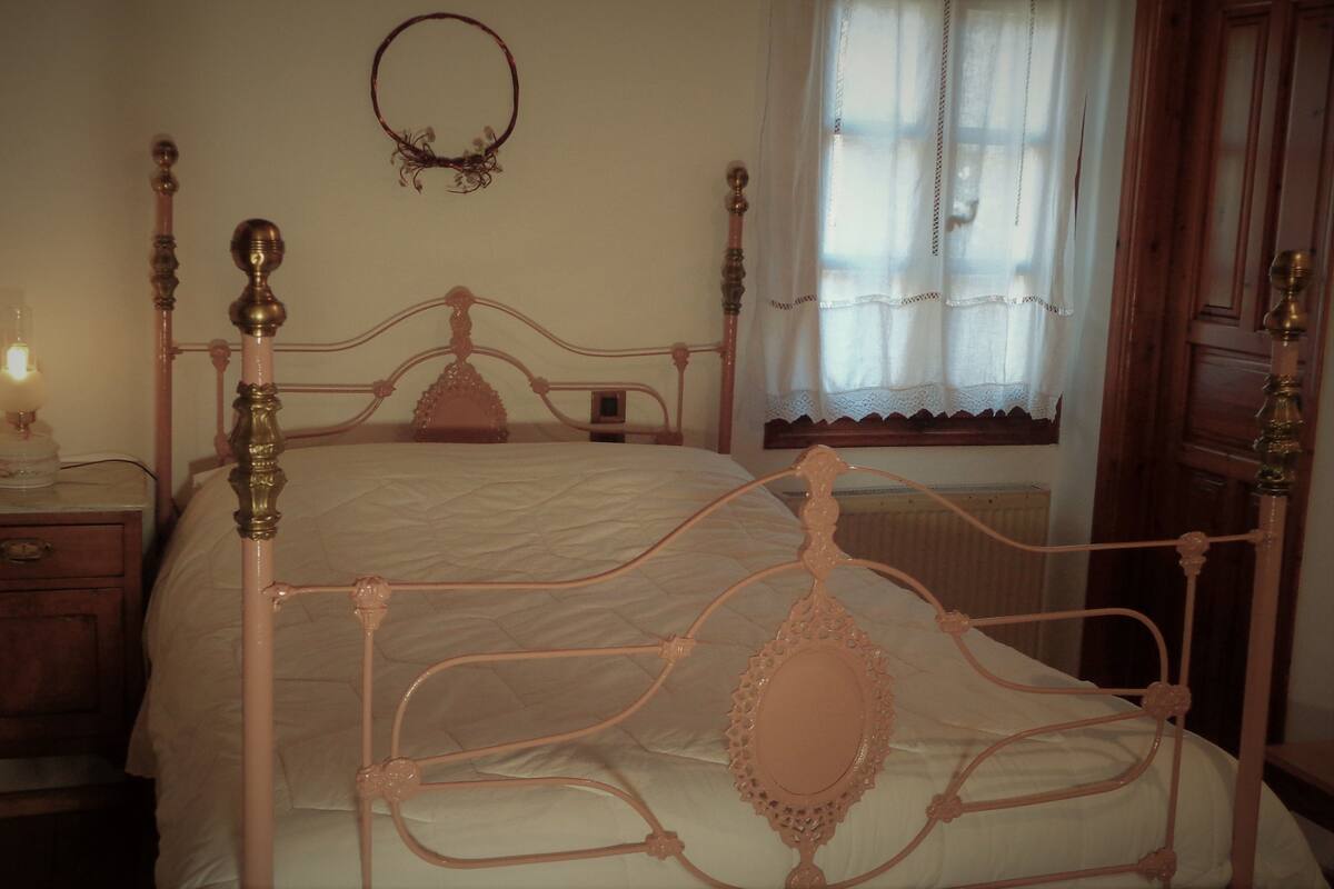 A bedroom with a four-poster bed, a bedside table with a lamp, and a window with curtains.