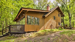Eine Holzhütte mit einer Terrasse und Schornstein, umgeben von Bäumen.