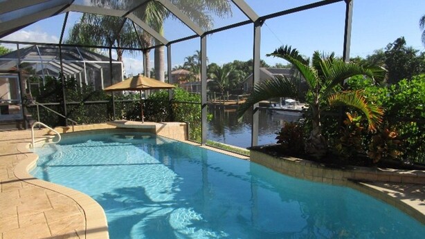 Una piscina interior con agua cristalina, rodeada por una zona techada con techo de vidrio, palmeras y vistas a una zona residencial.