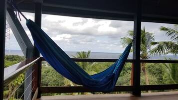 Una hamaca en una terraza de madera con vista al océano y palmeras.