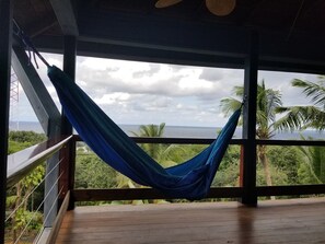 A hammock on a wooden deck with a view of the ocean and palm trees.