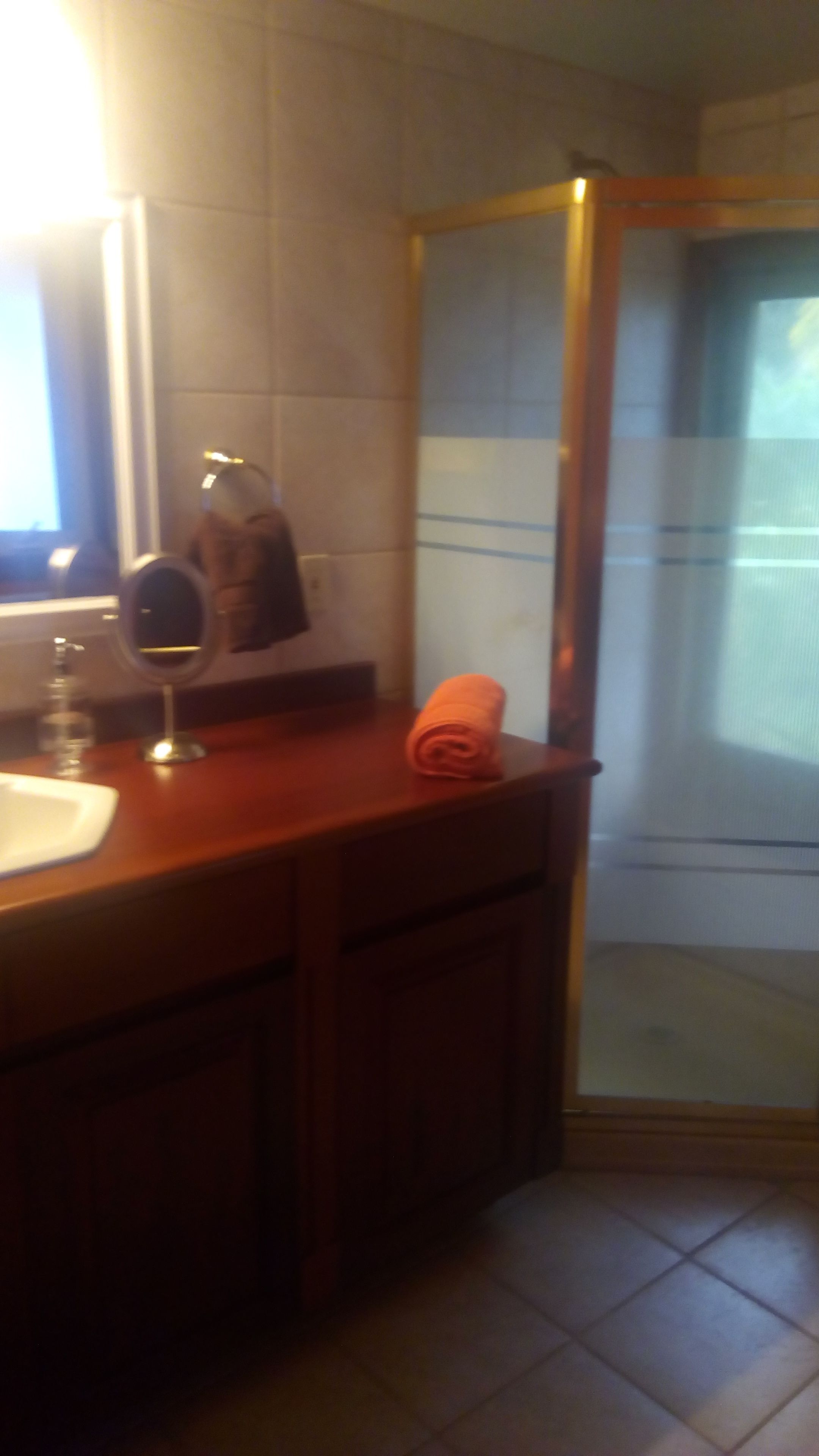 A bathroom with a wooden vanity, a mirror, a towel, and a shower area.
