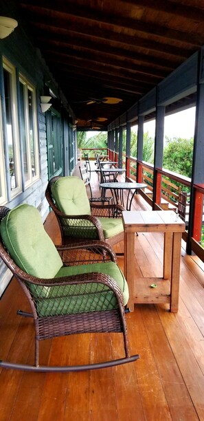 A covered outdoor seating area with wicker rocking chairs and a wooden table.