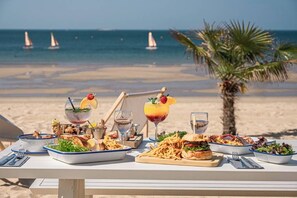A table set with various dishes and drinks on a beach with a palm tree and sailboats in the background. - Pop design apartment, renewed in 2008, terraces in the garden, heart of La Baule (La Baule-Escoublac)