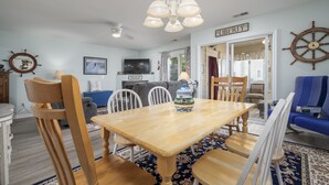 Un coin repas avec une table et des chaises en bois, un lustre, un téléviseur et une enseigne sur laquelle on peut lire « LIBERTÉ ».