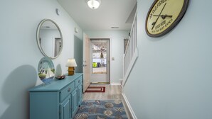 Un couloir avec une commode bleue, un miroir et une horloge au mur.