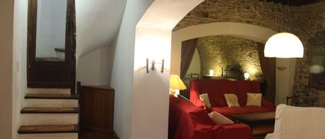 Quarto aconchegante com parede de pedra, um sofá vermelho, uma poltrona branca e uma escada.
