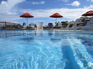 A clear swimming pool with lounge chairs and red umbrellas.