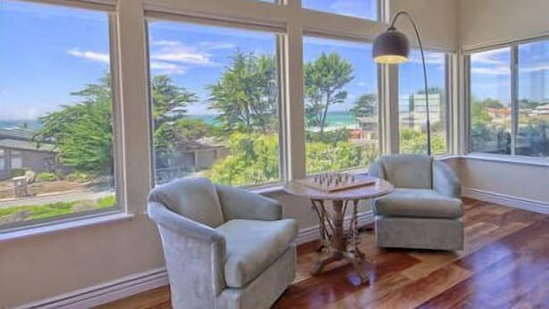 Una habitación amplia con ventanas grandes, dos sillones, una mesita y una lámpara.
