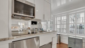 Eine moderne Küche mit Edelstahlgeräten, einem großen Fenster mit Jalousien und Blick ins Freie.