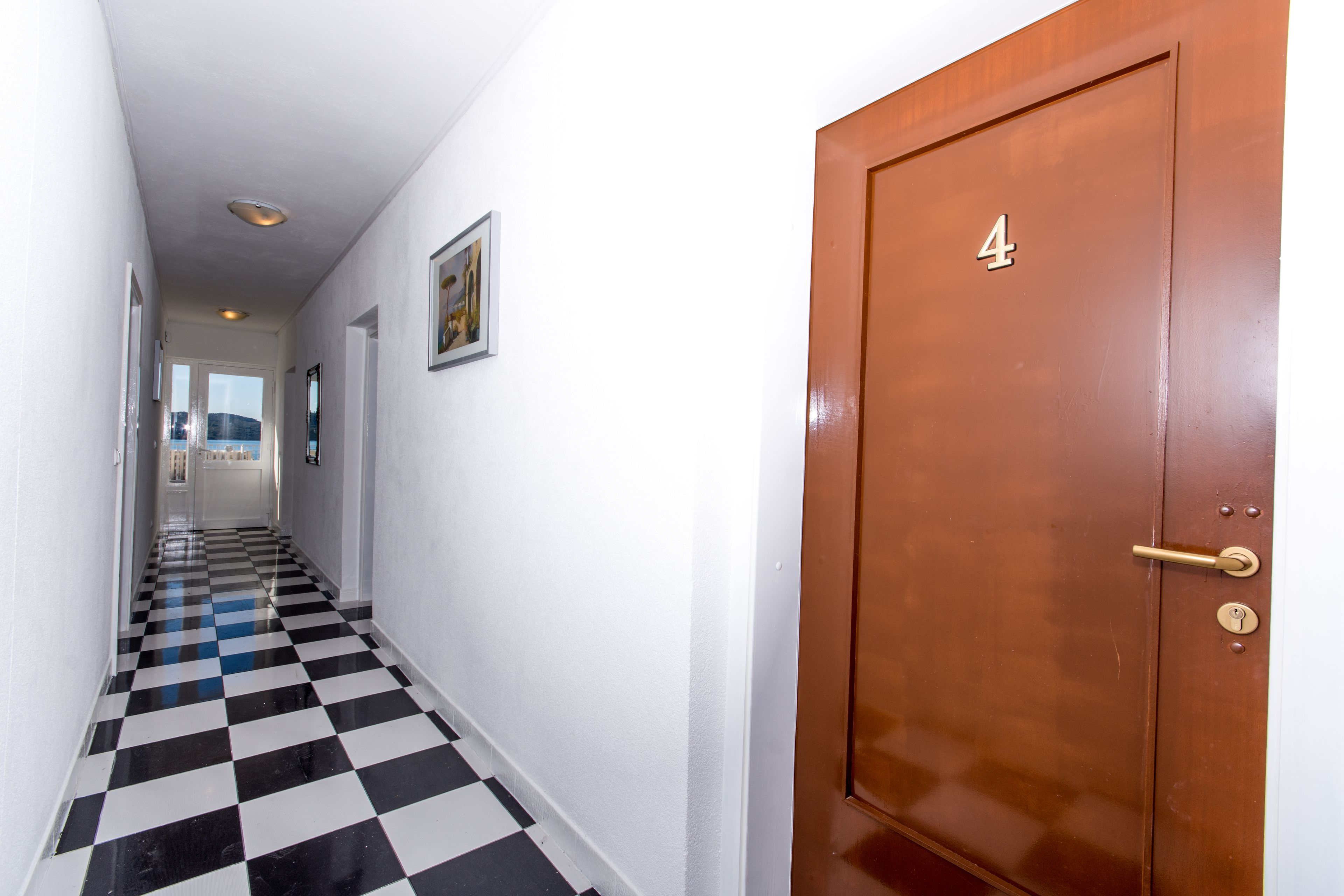 A hallway with a checkered floor, a door labeled with the number 4, and a framed picture on the wall.