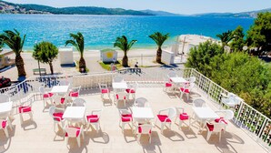 Un espace extérieur aménagé avec des tables et des chaises blanches, offrant une vue sur une plage et la mer.