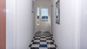 Un couloir doté d’un sol à carreaux, de murs blancs et d’une porte donnant sur un balcon avec vue sur la mer.