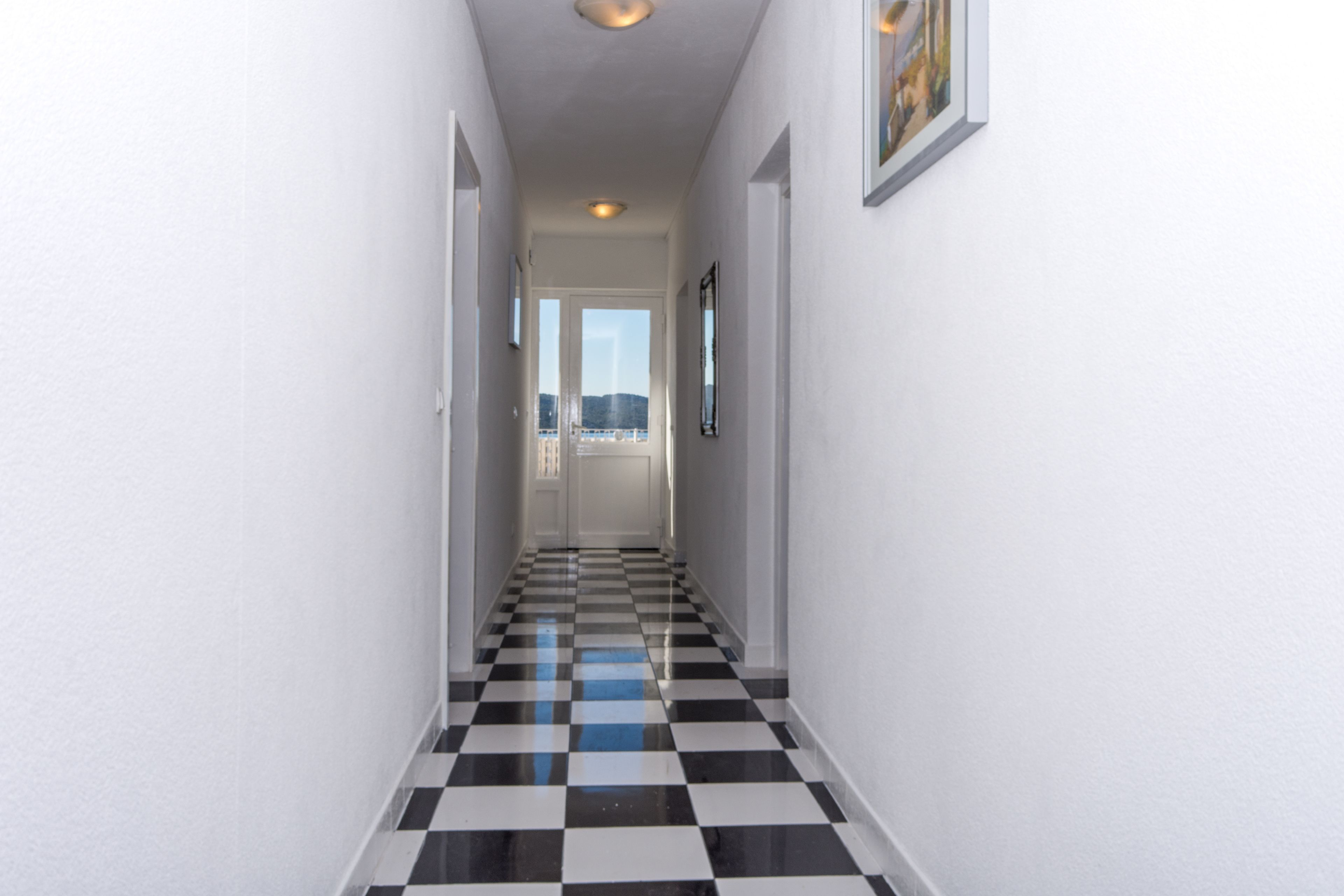 A hallway with a checkered floor, white walls, and framed pictures.