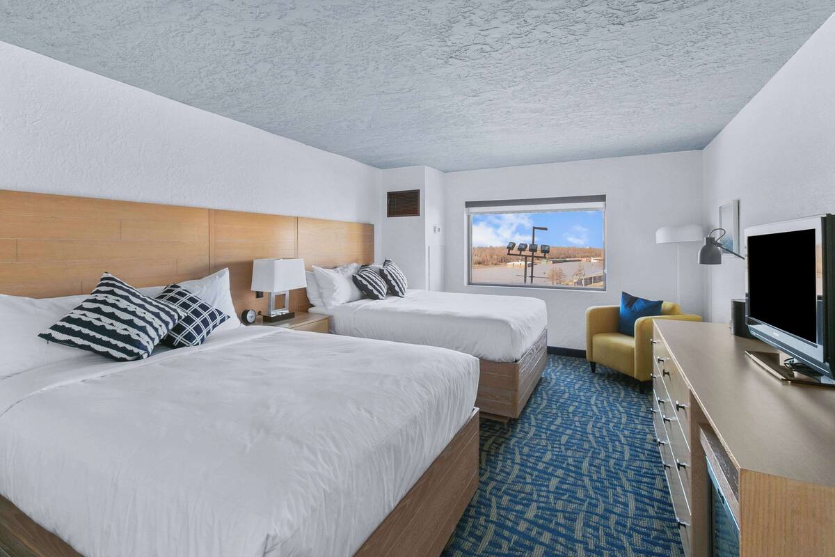 A hotel room with two beds, a TV, a desk, and a window with a view of a landscape.