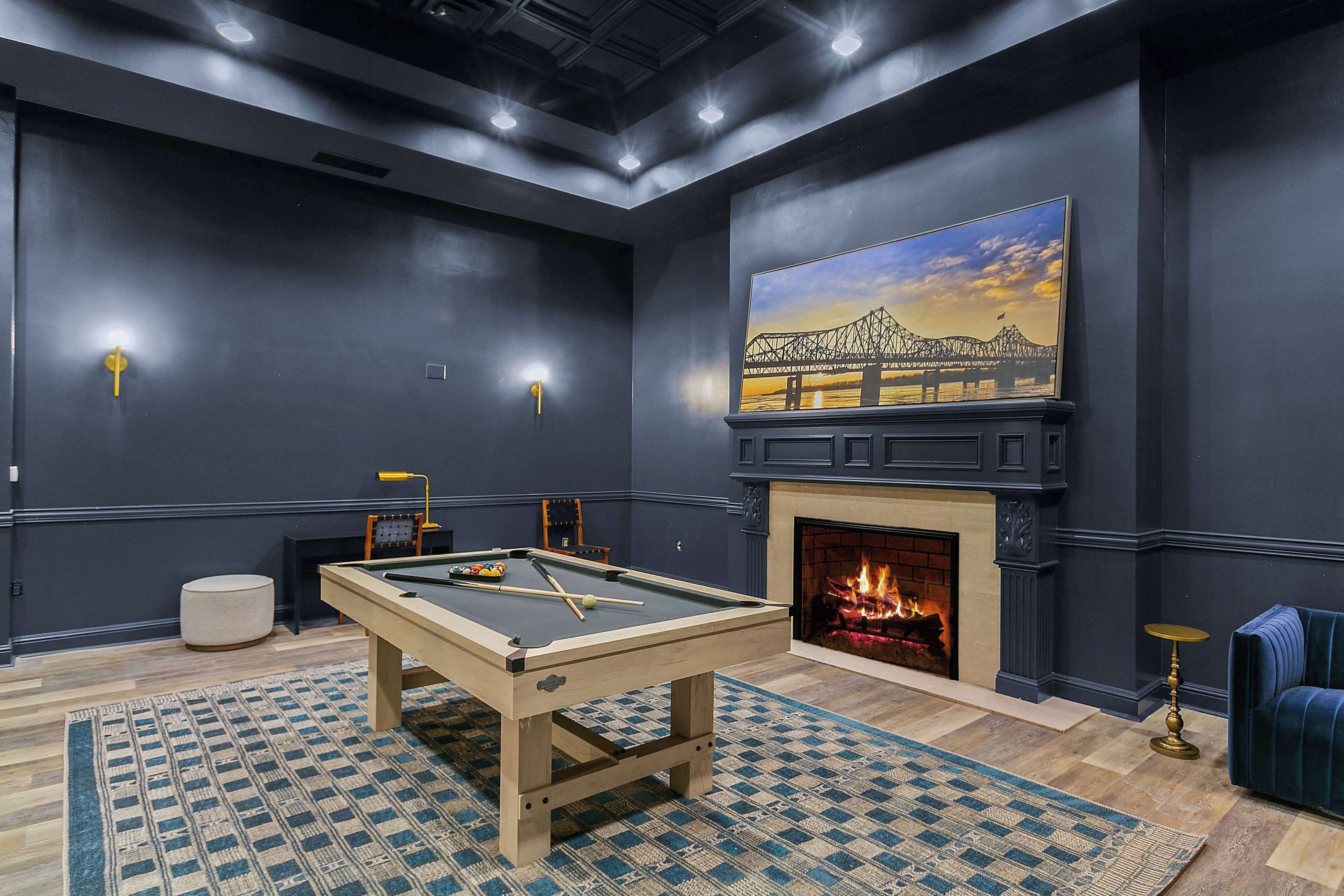 A room with a pool table, a fireplace, and a painting of a bridge.
