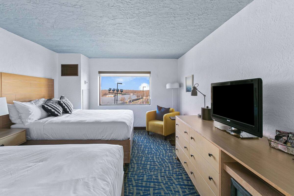 A hotel room with two beds, a desk with a TV, a chair, and a window with a view of a cityscape.