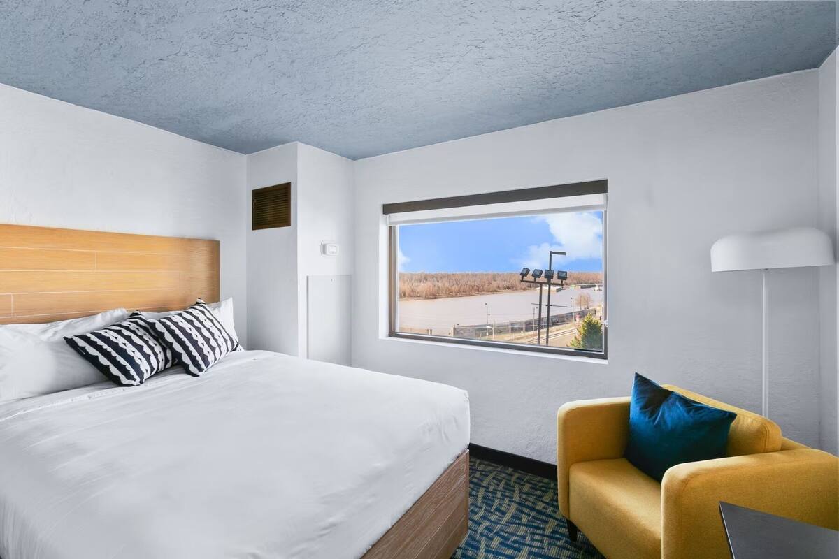 A hotel room with a bed, a sofa, a window with a view, and a lamp.