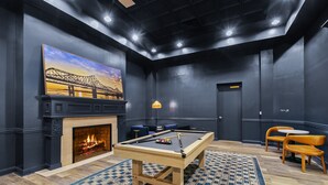 Une table de billard agrémentée d’un foyer, une table de jeu de flipper et un grand tableau représentant un pont.