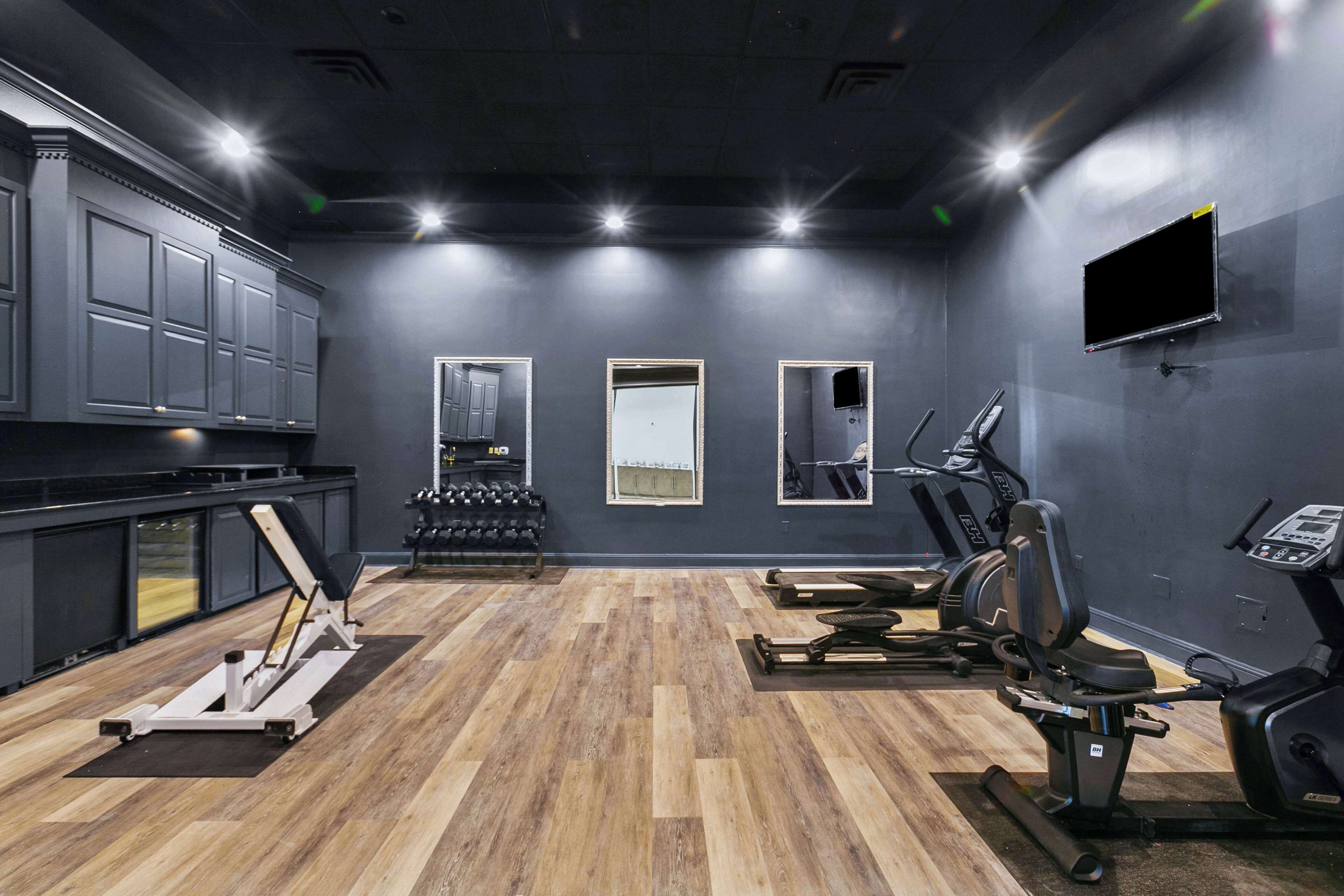 A gym with exercise equipment, a wall-mounted TV, and a row of dumbbells.