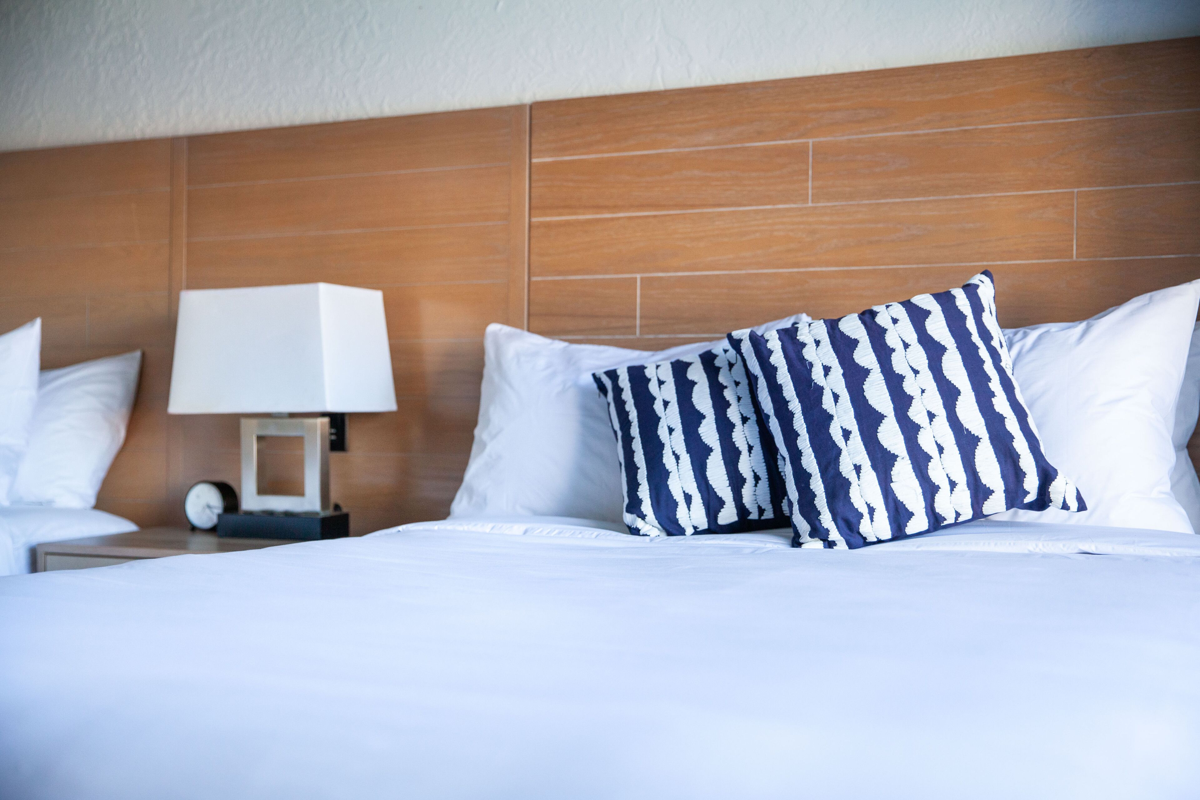 A hotel room with a wooden headboard, white bedding, and a patterned pillow.