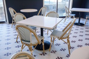 A room with a white table surrounded by wicker chairs, a patterned floor, and a view through a large window. - Mulberry, a Wyndham Hotel (Vicksburg)