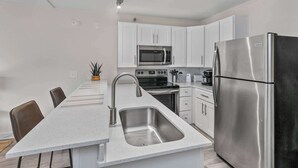 Une cuisine moderne avec des meubles blancs, des appareils en acier inoxydable, un grand îlot central doté d’un évier et un coin repas avec des chaises.