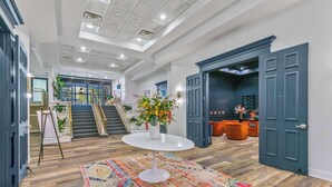 Un hall d’entrée spacieux, avec une grande table blanche au centre, un tapis aux couleurs vives et un escalier menant aux étages supérieurs.