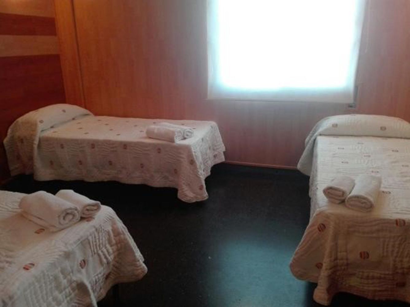 Ein Zimmer mit zwei Einzelbetten, jeweils mit einem kleinen Tisch und einem zusammengerollten Handtuch.