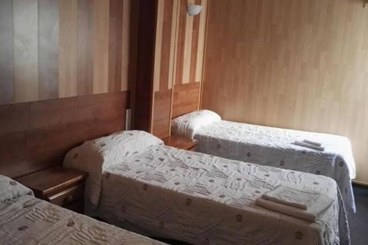 Ein Zimmer mit drei Einzelbetten, Holzkopfteilen und einem kleinen Nachttisch mit einer Lampe.