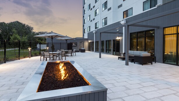 A modern outdoor patio with a rectangular fire feature, seating areas, and a building with large windows.