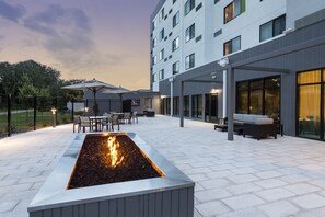 A modern outdoor patio with a rectangular fire feature, seating areas, and a building with large windows. - Courtyard by Marriott Tampa Northwest/Veterans Expressway (Tampa)