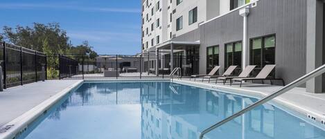 Un hotel moderno con piscina, tumbonas y una zona exterior cubierta.