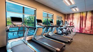 A gym with treadmills, exercise bikes, and a large window providing a view of the outdoors.