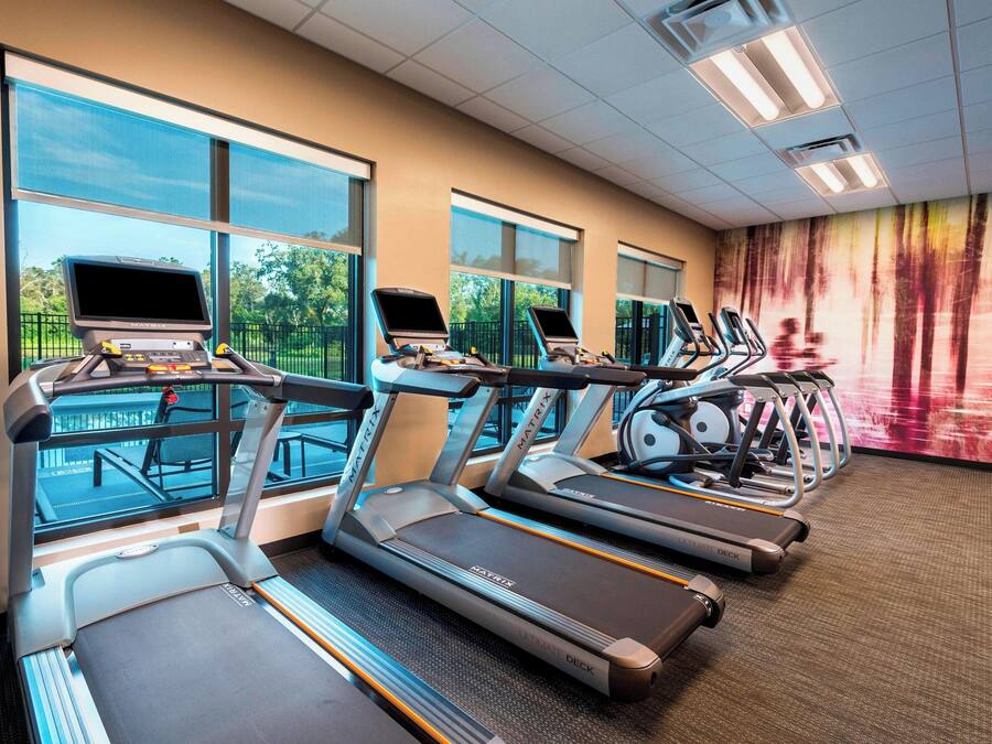 A gym with treadmills, exercise bikes, and a large window providing a view of the outdoors.