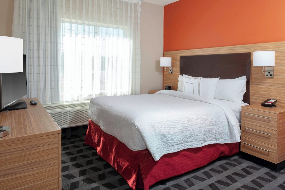 Una camera d'albergo con un letto, due comodini, una televisione e una finestra con tende.