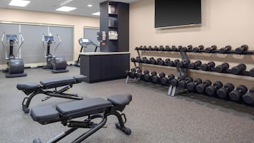 A gym with treadmills, a bench press, and a rack of dumbbells.