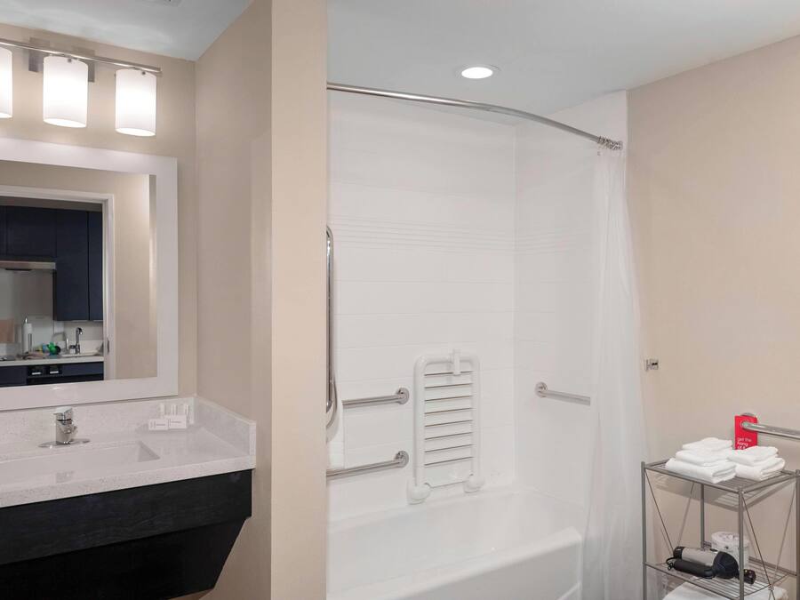 A bathroom with a white bathtub, a vanity with a mirror, and a towel rack.