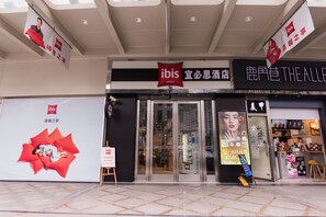A hotel entrance with glass doors, a sign for ibis hotels, and a large advertisement on the left. - Ibis Shanghai Changshou (Shanghai)