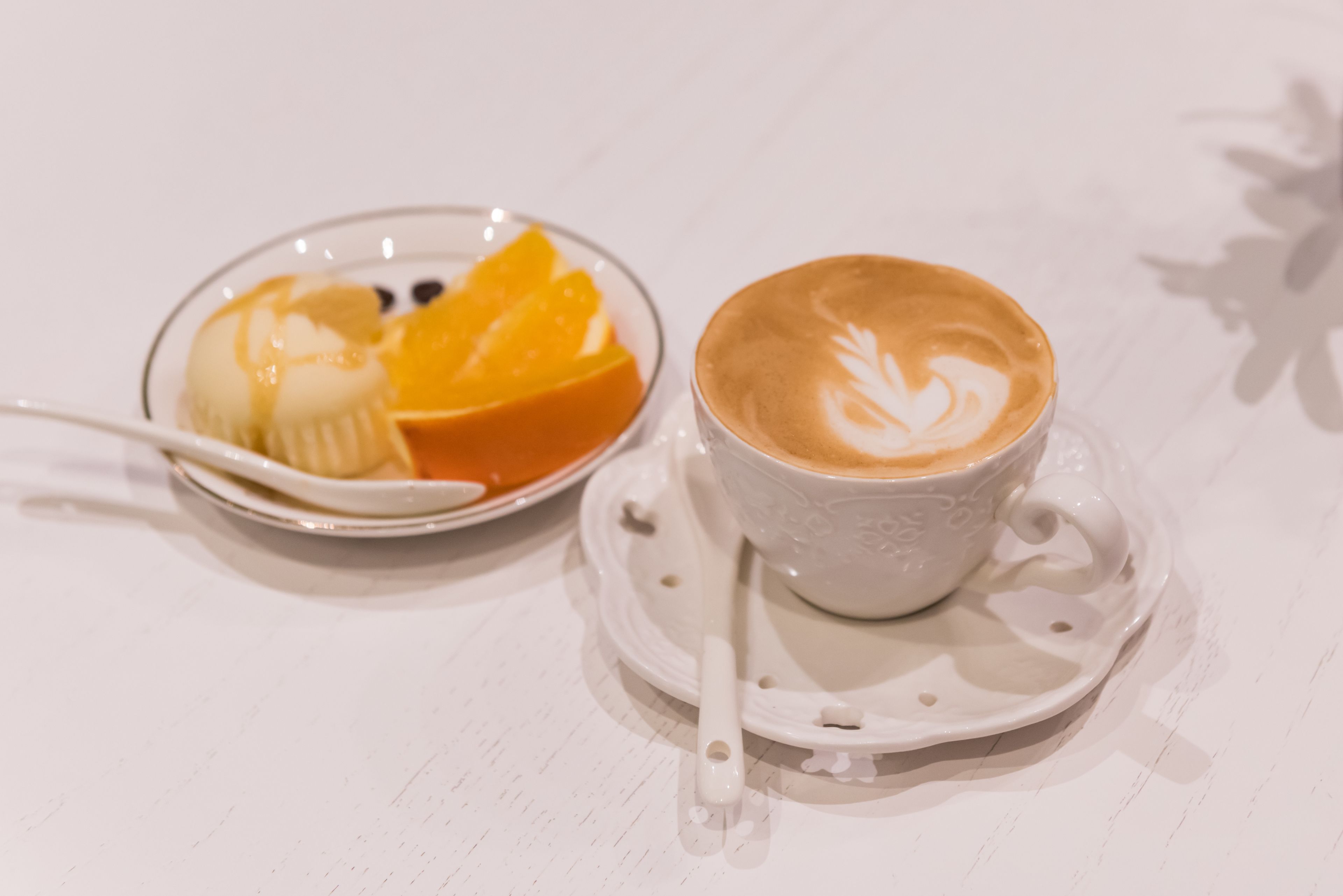 A white table with a cup of coffee and a plate of food.