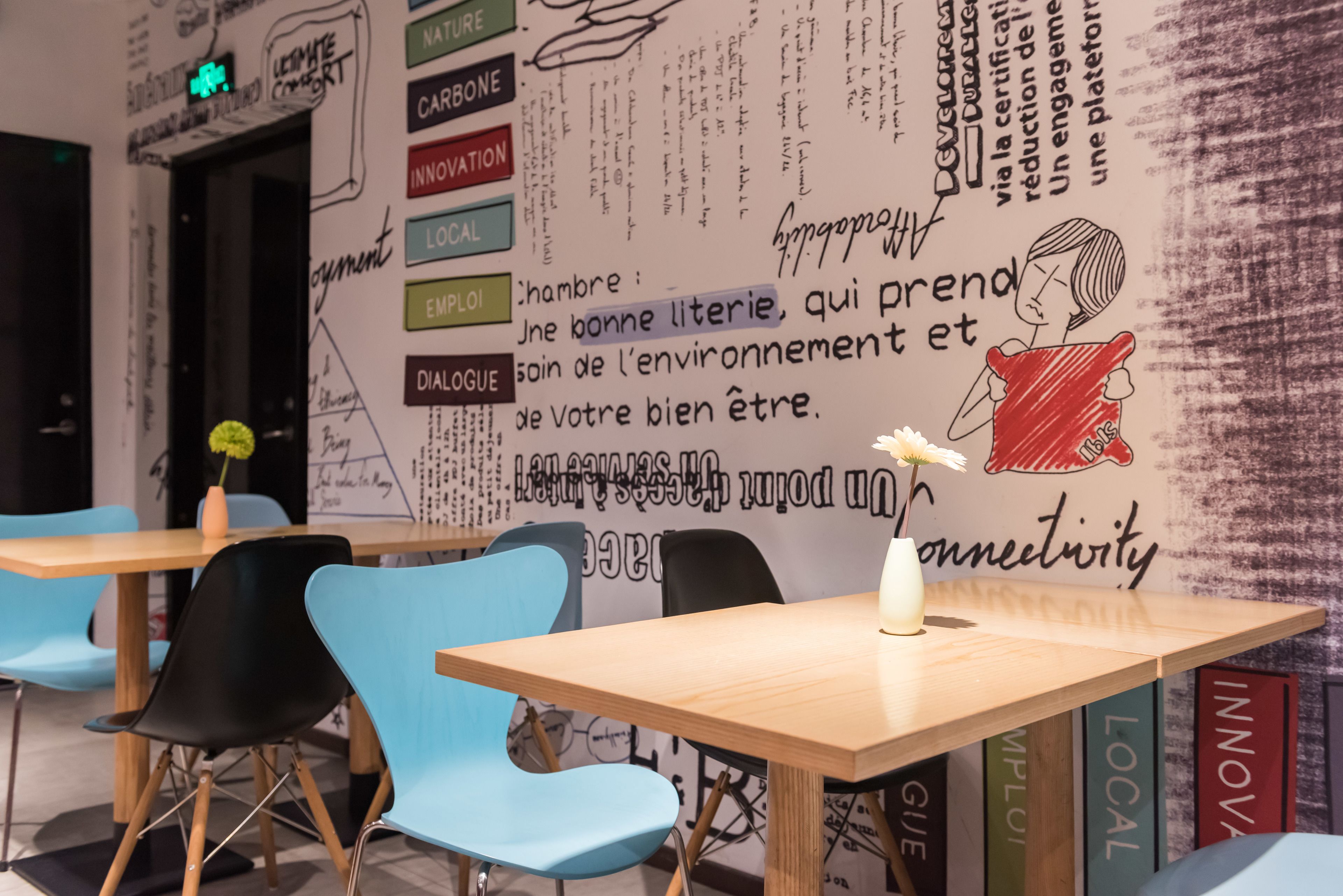 Un café moderne avec une table en bois et des chaises bleues, agrémenté d’un mur orné de citations inspirantes et d’un panneau néon.