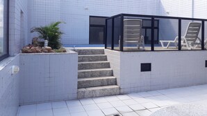 Uma área externa moderna com paredes revestidas de azulejos, um conjunto de escadas e um espaço de estar envidraçado com poltronas de descanso.