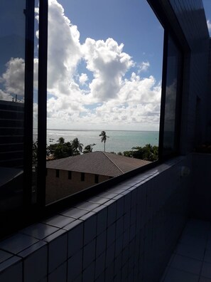 Une vue depuis une fenêtre donnant sur une plage, avec un ciel dégagé et quelques nuages.