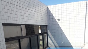 Uma piscina com água azul cristalina, rodeada por paredes de azulejos brancos e uma janela com estrutura preta.
