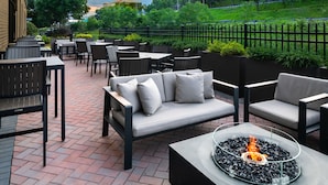 An outdoor patio with seating arrangements, including a sofa and chairs, and a fire feature.