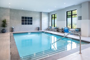 A modern indoor swimming pool with clear water, a tiled floor, and a seating area with chairs and a table. - Fairfield Inn & Suites by Marriott Boston Waltham (Waltham)