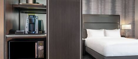A hotel room with a bed, a minibar, and a coffee machine.